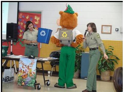 Sustainable Operations team member Maritza Huerta (L) and Tamberly Conway of Conservation Education explain Woodsy Owl’s motto to K through 2 students at Braddock Elementary School. 