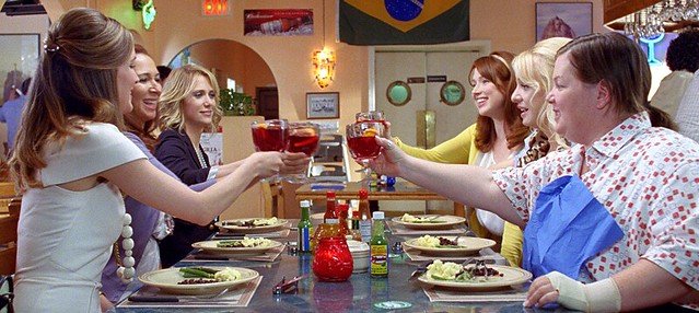 the cast of Bridesmaids, six women, around the table at a restaurant.
