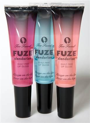 Three Fuze lip glosses standing upright against a white background. They are liquid glosses meant to be squeezed from the tube and are in clear plastic containers with black caps. They are transparently pink, blue and orange respectively, with black letters on the front that read "Too Faced: FUZE slenderize GUILT FREE LIP GLOSS, Always on the lips, Never on the hips".