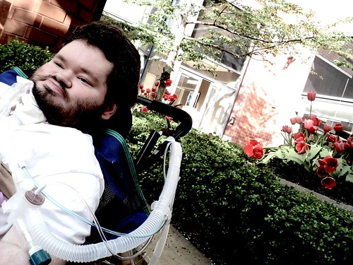 Nick sitting in front of flowers outside, in wheelchair