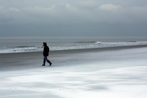 Pessoa encapotada andando na praia nevada de Scheveningen, Holanda
