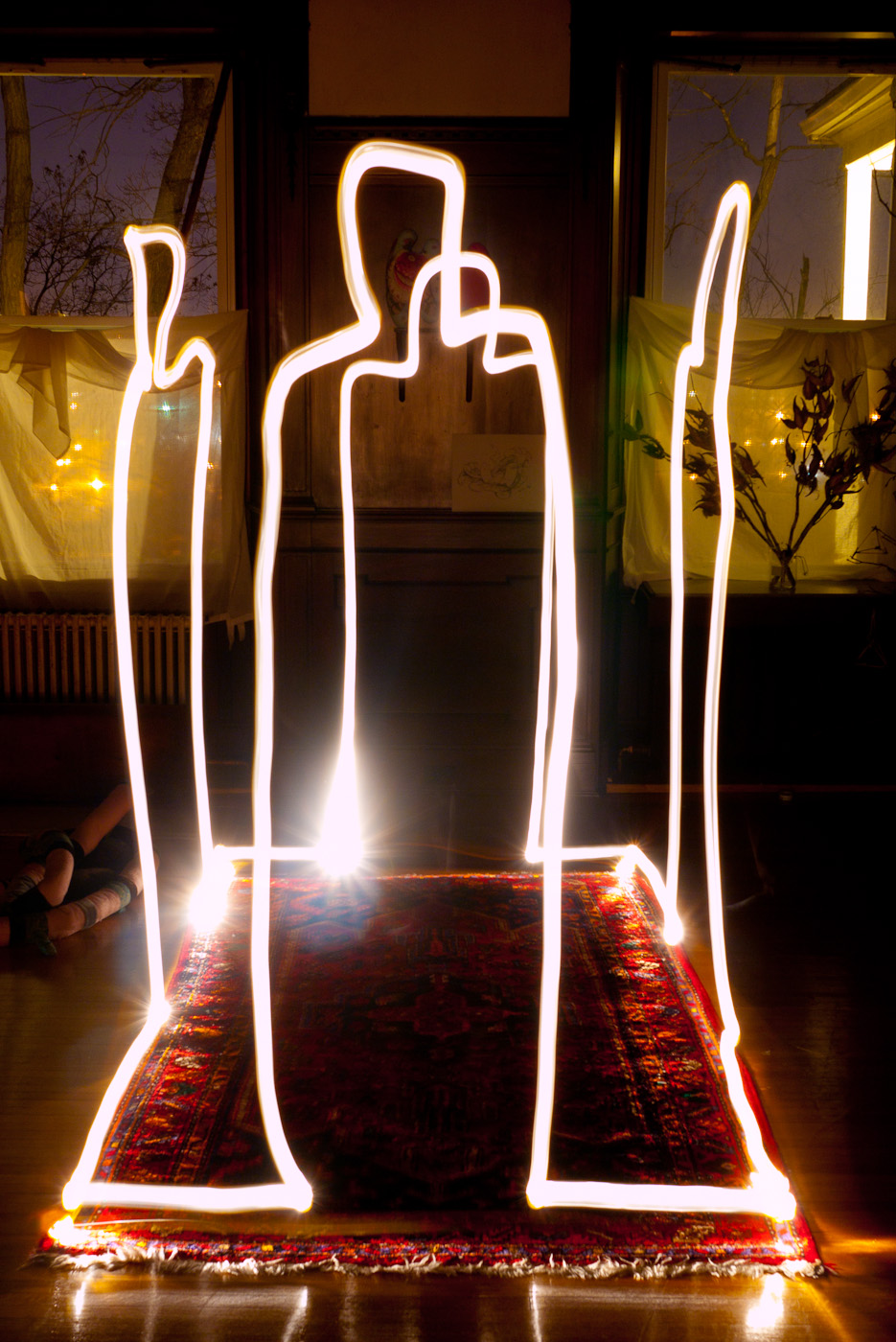 Light trails drawing of four figures standing in a rectangle that looks like a house.