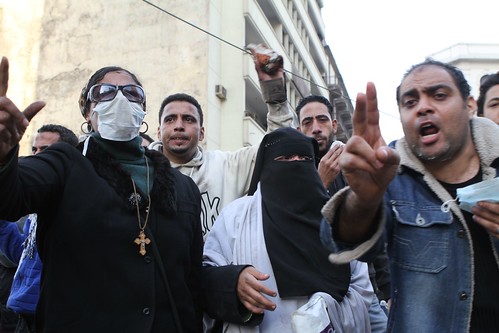 امرأة مسيحية و أخرى مسلمة في نقاب بينما كان قسم الشرطة المقابل يطلق النار بالذخيرة الحية على المتظاهرين في 28 يناير. تصوير سارة كار. 