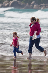 Mother and daughter scamper across the wet sand and breaking waves