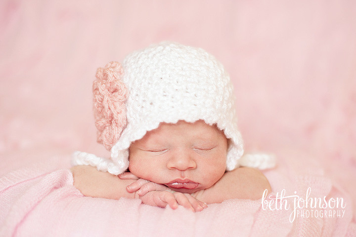 newborn baby girl in white hat on pink ruffled blanket