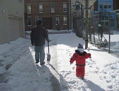Dad and toddler walk in the snow, shovels in hand