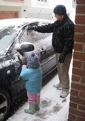 little girl and dad sweep snow off a black car
