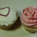 Vanilla cupcakes, one with sugar pearl heart outline and the other with pink-tinted icing and tiny heart sprinkles