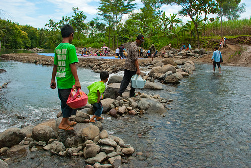 Warga Girimulyo menyebrangi sungai kayangan membawa makanan nasi berkat untuk disantap bersama pada upacara adat Kembul Sewu Sedulur