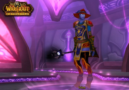A draenei shaman with purple skin and glowing eyes wears her drinking hat, a tabard, pauldrons, a belt, long stocking-like leg coverings, and what appears to be a red pair of underpants. She is wielding a magical staff.
