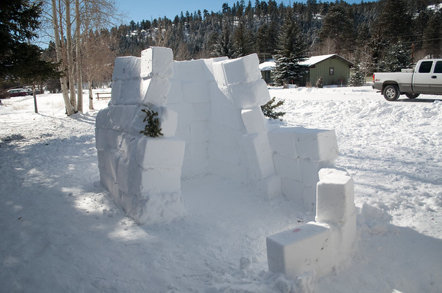 Half an igloo standing in the front yard, it has three big walls made of giant snow cubes and a tiny quarter wall on its way to winding around it in attempts to make a hallway. There is no roof on top and the walls are leaning in towards each other.
