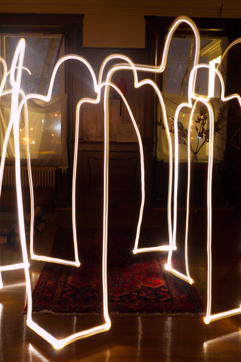 Light trails drawing of figures standing randomly arranged in a room.