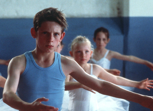 Billy Elliot, a white boy in a blue tank top, in a ballet class