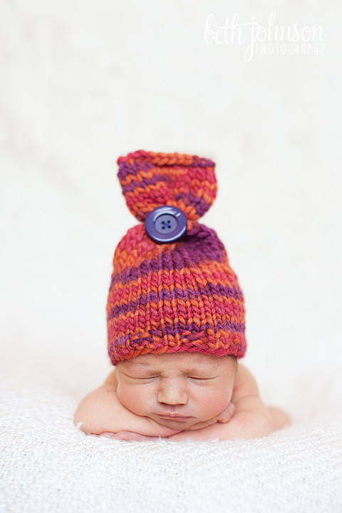 newborn baby girl in purple and orange button hat
