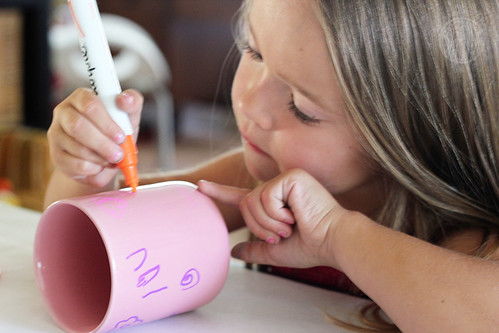 Child painting a cup with a marker 