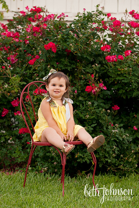 one year old baby girl in front of roses in red chair