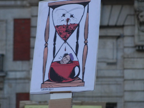 Cartel: "Reloj de arena y Gadafi ahogándose con el paso del tiempo"