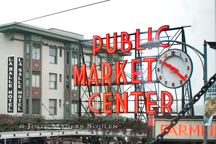 a close up rainy photo of the Pike Place Market in Seattle highlighting the bright red market sign and clock