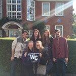 Students and professor pose in front of a house while holding a Westminster Flag