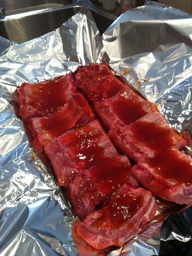 Baby back ribs covered in sauce on foil-lined baking sheet