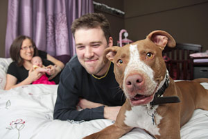Couple with a baby and a dog sitting on their bed